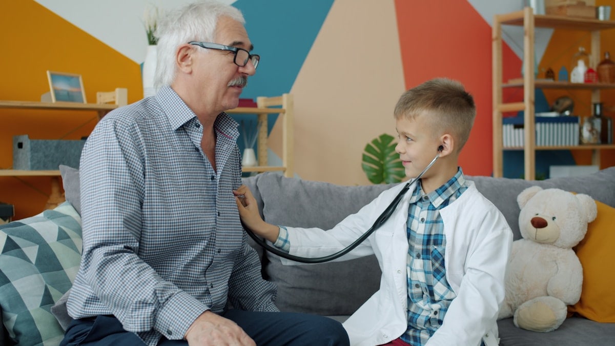 Adorable child is playing with grandfather examining with stethoscope in apartment having fun together indoors. Medicine, childhood and leisure activities concept.